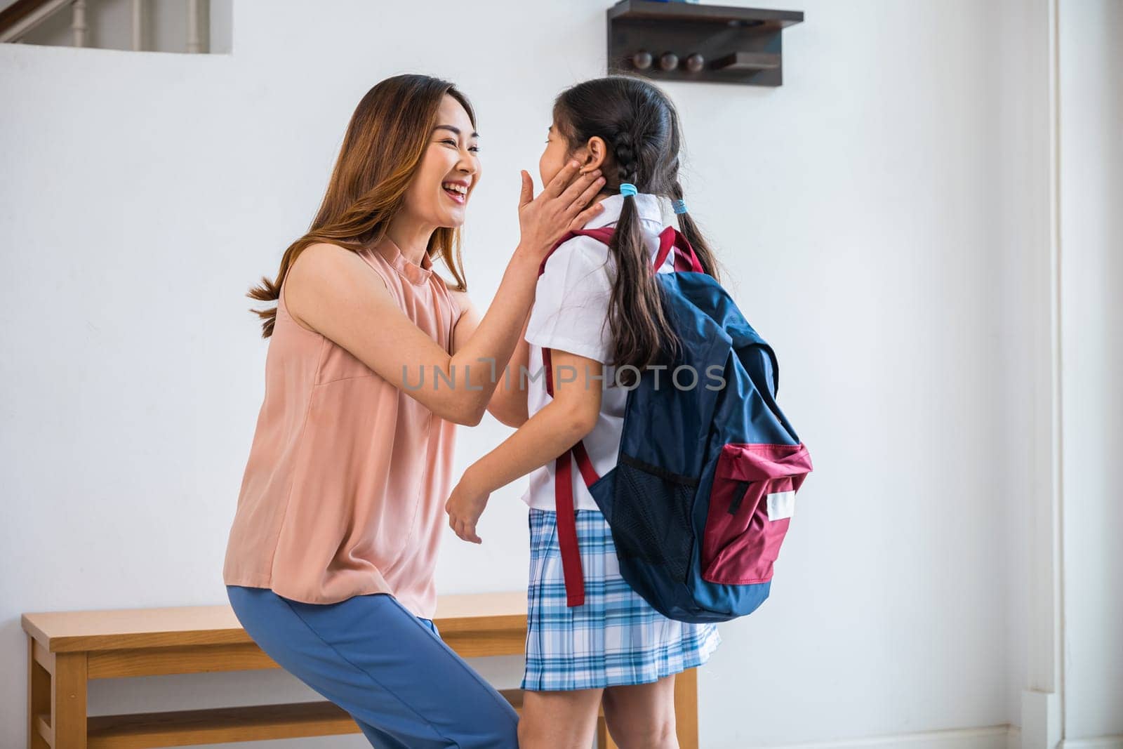 Asian mother hugging her daughter saying goodbye before go to school at home, loving mom and schoolgirl with backpack before first day, parents and child little girl