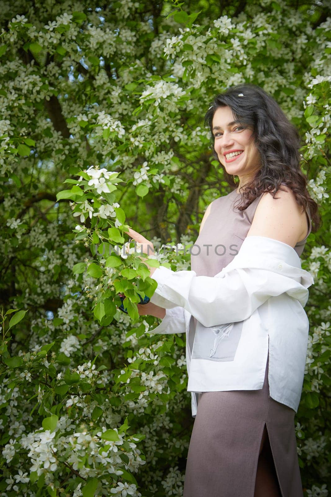 Joyous brunette woman near Blossoms of apple tree in a Spring Garden outdoors. Concept of face and body care. The scent of perfume and tenderness by keleny