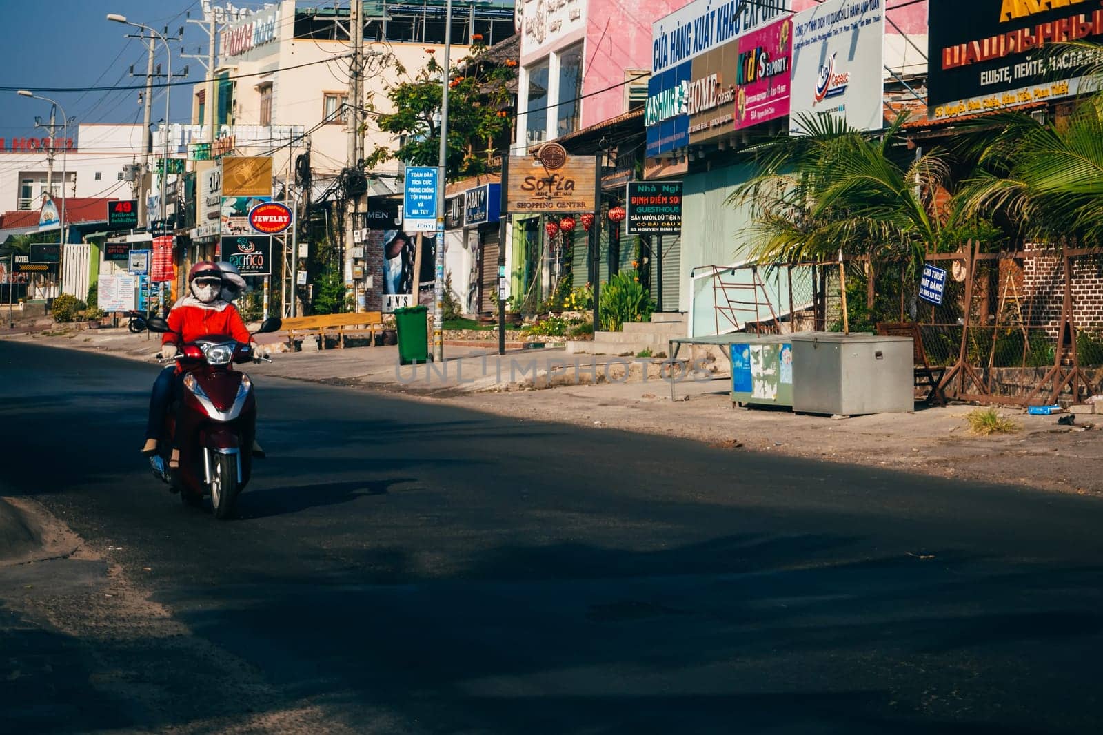 MUI NE, VIETNAM - CIRCA MARCH 2017: People riding motorbikes on the road against the background of advertising and shops