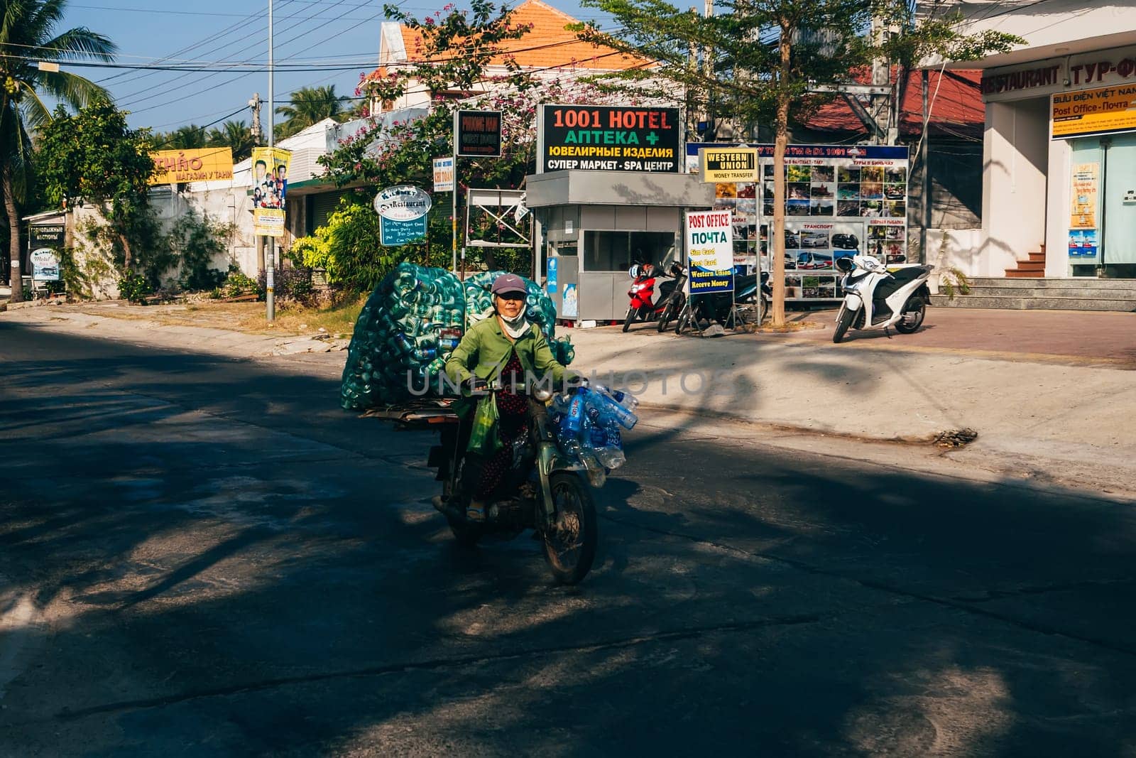 MUI NE, VIETNAM - CIRCA MARCH 2017: Elderly woman riding a motorbike and carries empty bottles of beer and water
