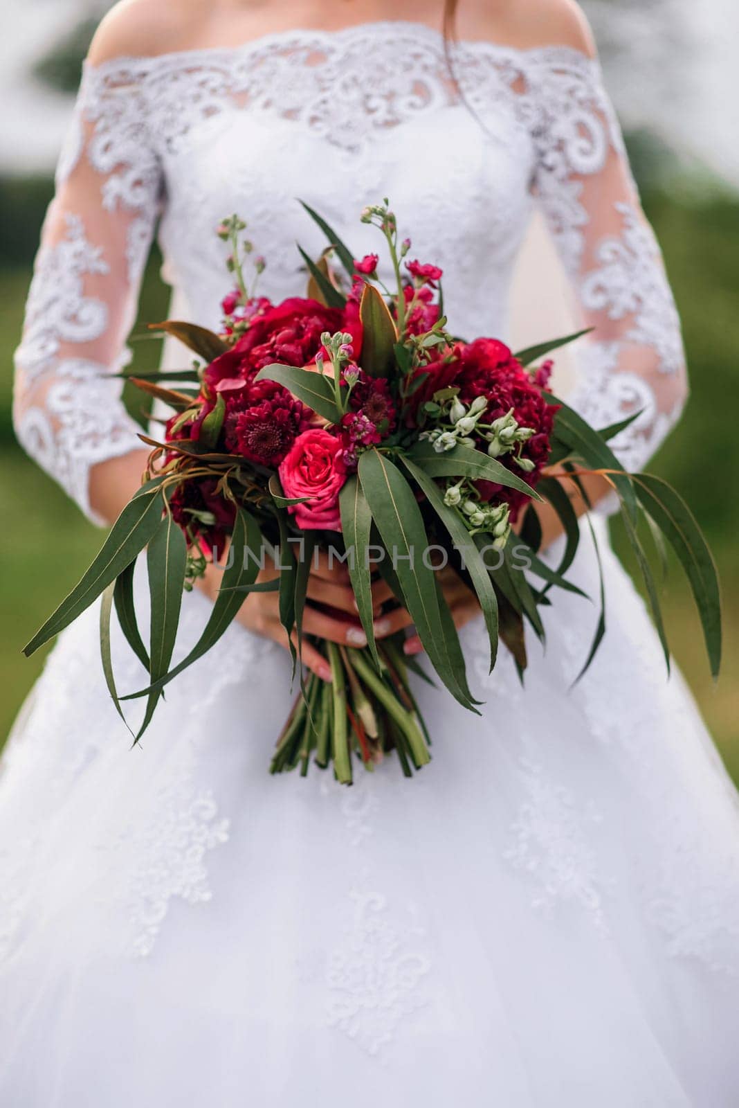 wedding bouquet with red peonies in the hands of the bride in a white elegant dress