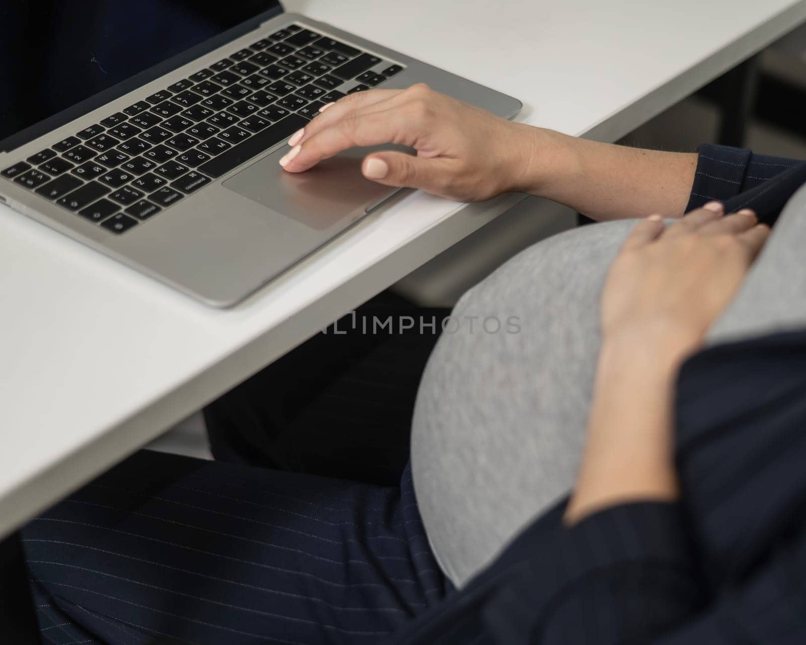 A pregnant woman works on a laptop in the office. Close-up of the tummy