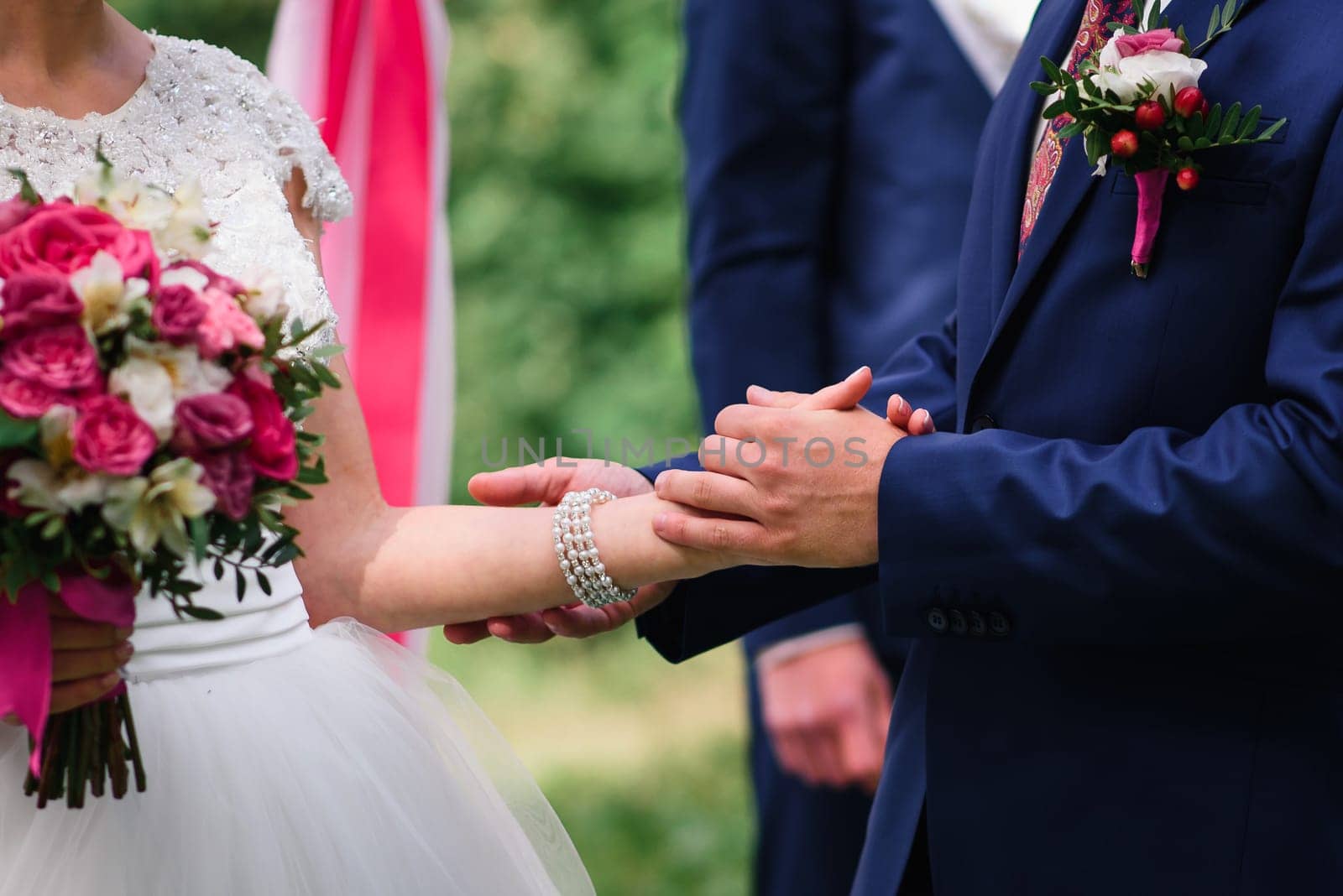 groom in a blue suit holds the bride's hand in a white dress at the wedding ceremony