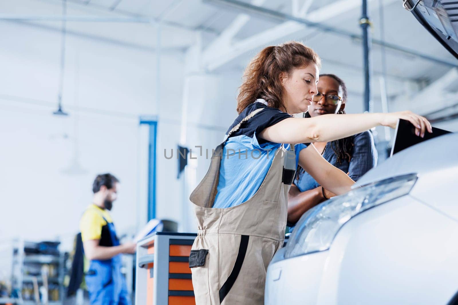 Efficient mechanic at auto repair shop conducts annual vehicle checkup, informing client about needed engine replacement. Automotive expert talks with customer after finishing car maintenance