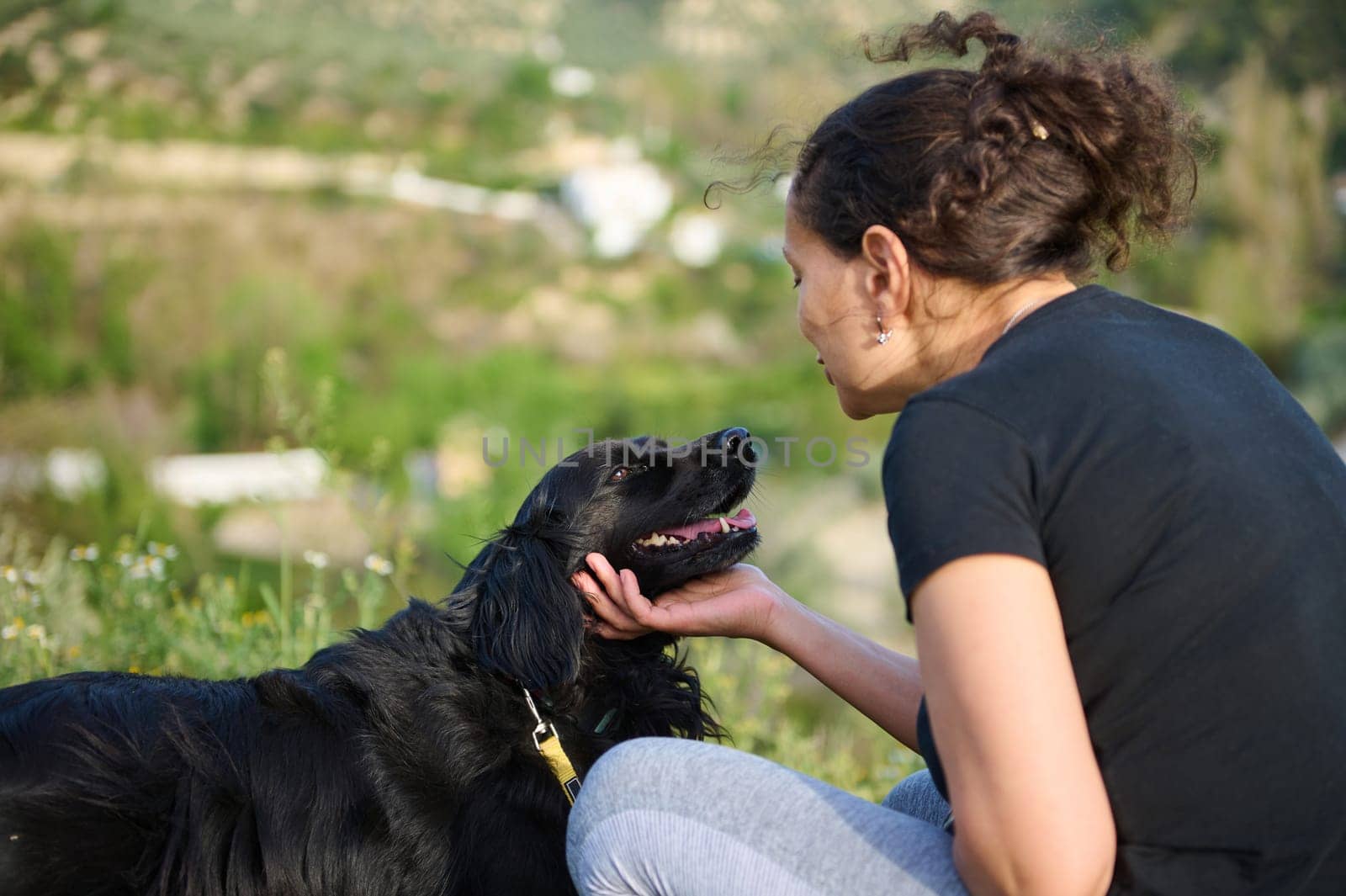 Authentic portrait of an affectionate young woman embracing pet dog in the nature. Happy female enjoying spending time with her cocker spaniel outdoors