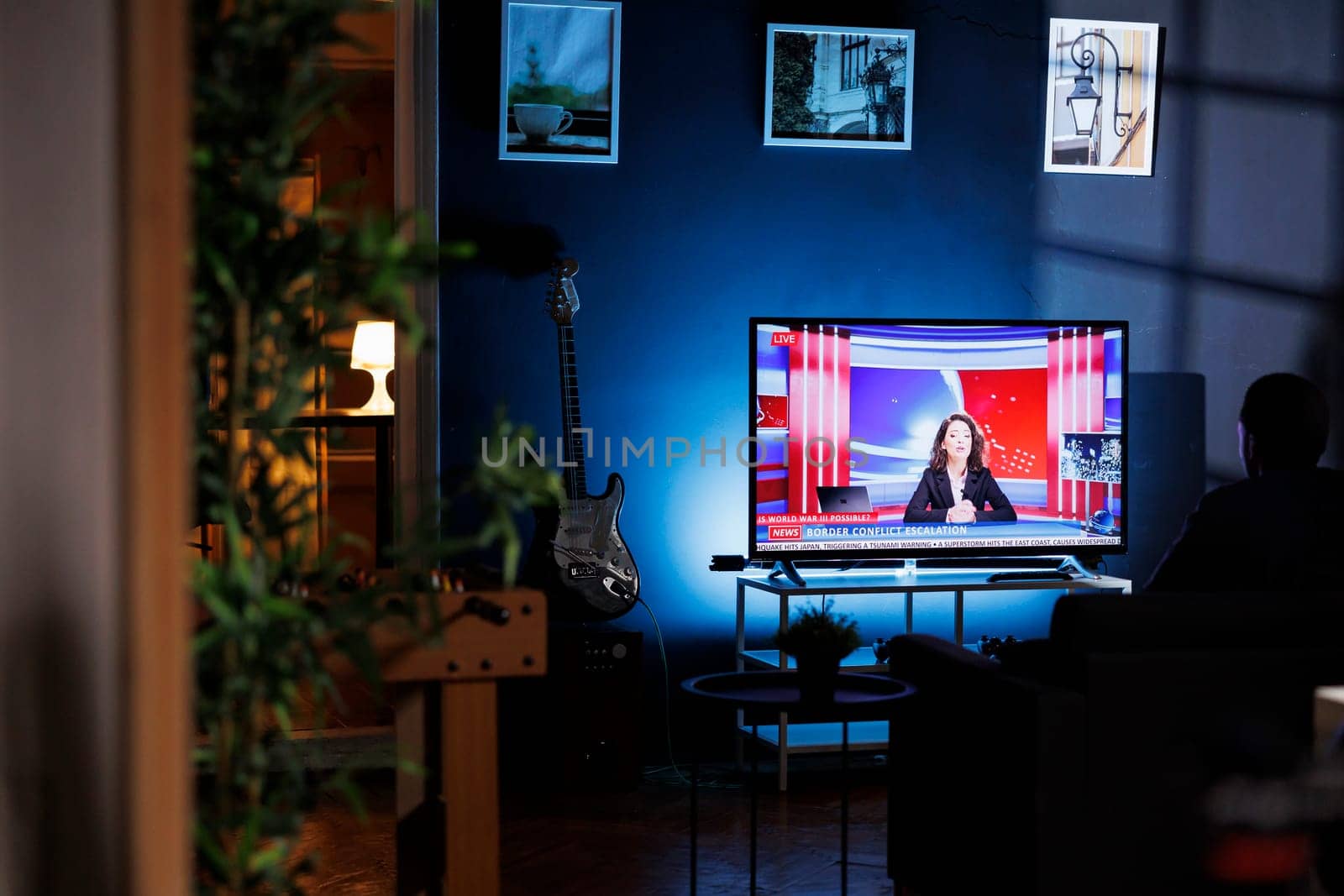 Relaxed person watching breaking news on television at night, chilling on sofa in living room and watching tv program. Young adult listening to media information on global network.