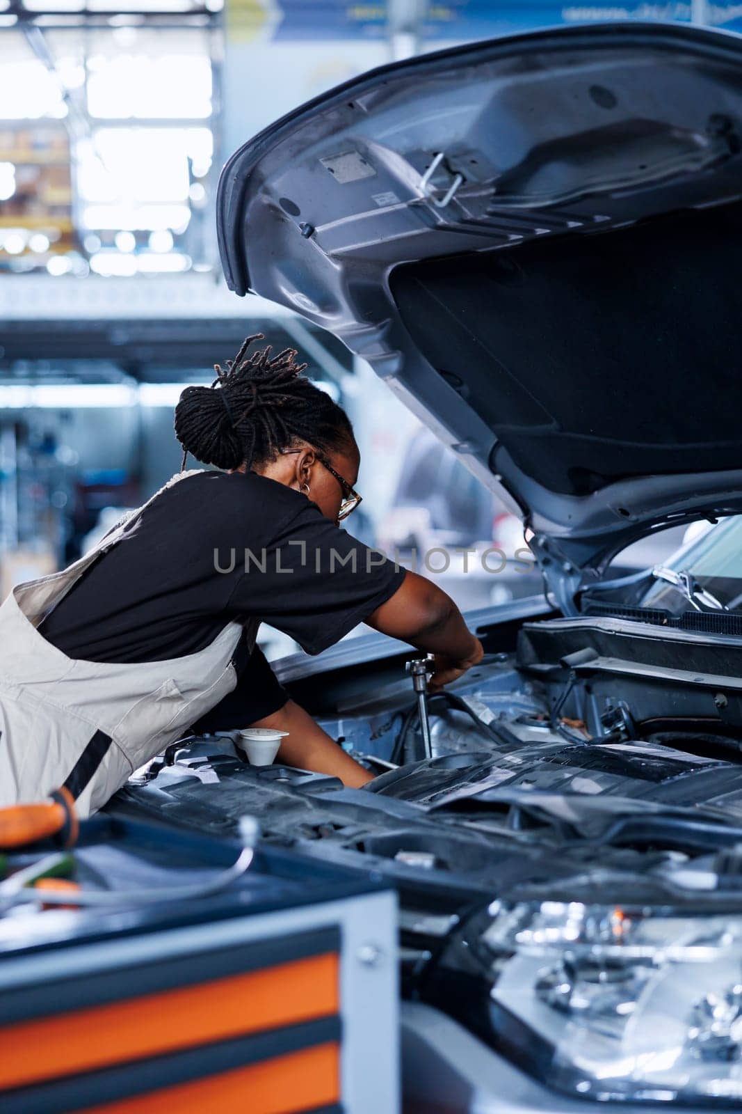 Car service technician expertly examines engine using advanced mechanical tools, ensuring flawless automotive performance and safety. African american woman in garage conducts routine vehicle checkup