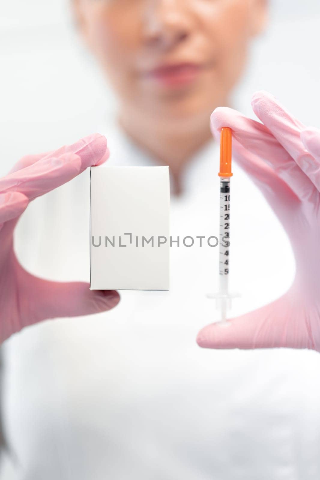 Female cosmetologist in pink gloves showing skin lifting injection and mock up drug box. Crop blur woman dermatologist demonstrating product mockup in clinic. Free space for advertisement.