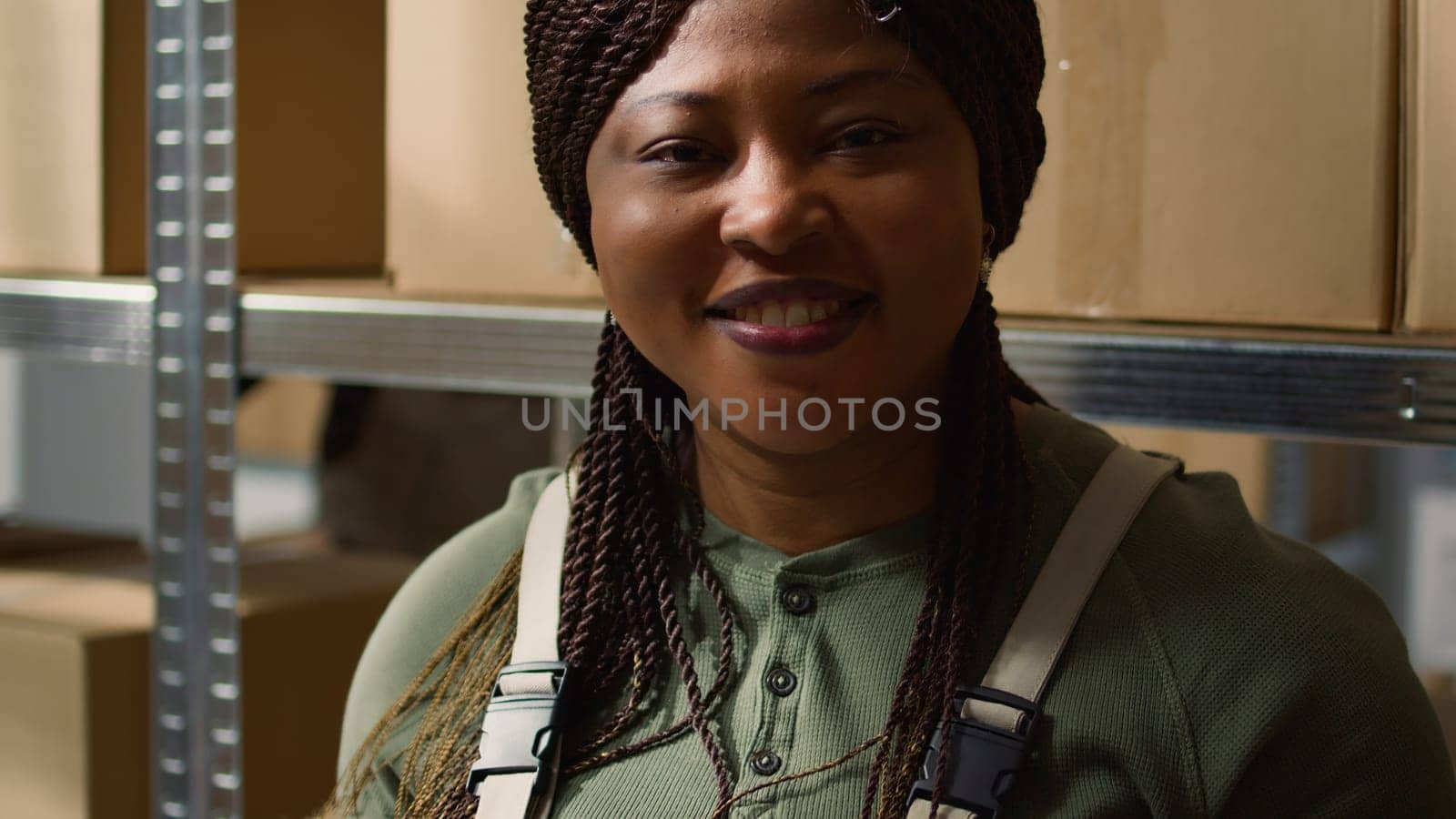 Portrait of cheerful african american warehouse supervisor inputing updated products info online, standing between retail storage venue cabinets indentifying parcels ready for shipping, close up