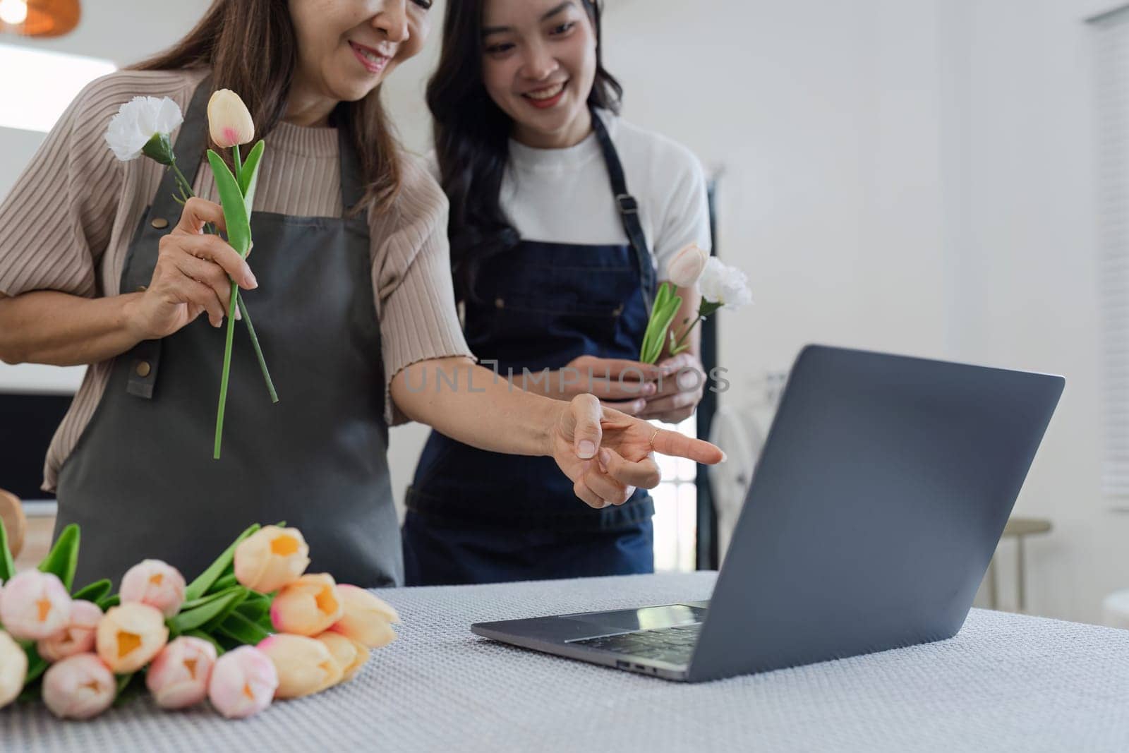 mother and daughter arrange flowers together as a hobby. mother and daughter spend free time doing flower arranging activities together and looking at laptop.