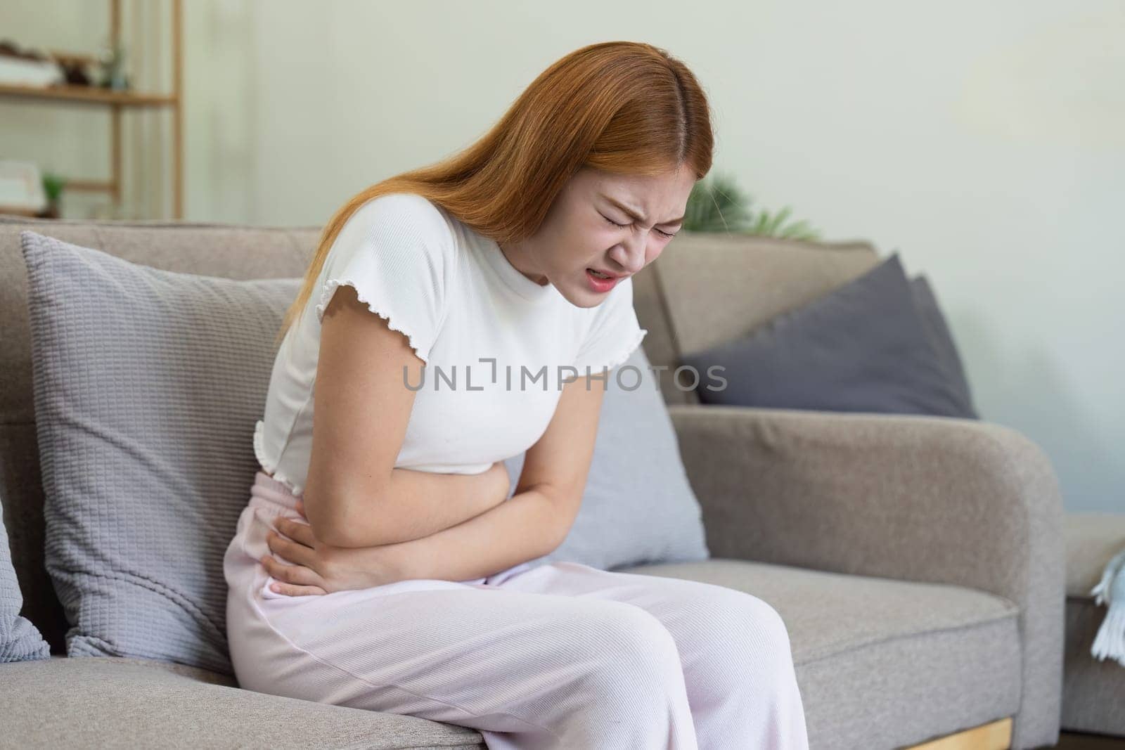 asian woman suffering from stomach ache, undergoing belly pain and discomfort, suffer from menstruation.