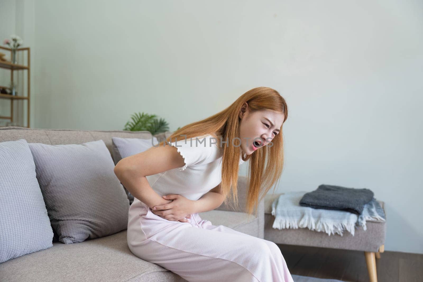 asian woman suffering from stomach ache, undergoing belly pain and discomfort, suffer from menstruation.