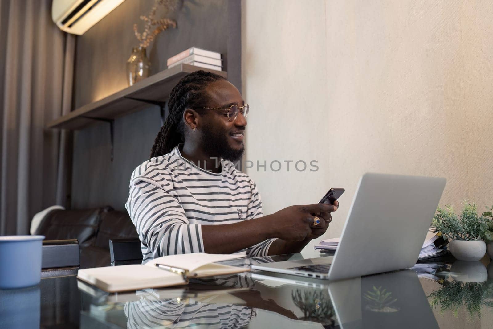 Young African American business man working with laptop and mobile on desk at home. work from home concept.