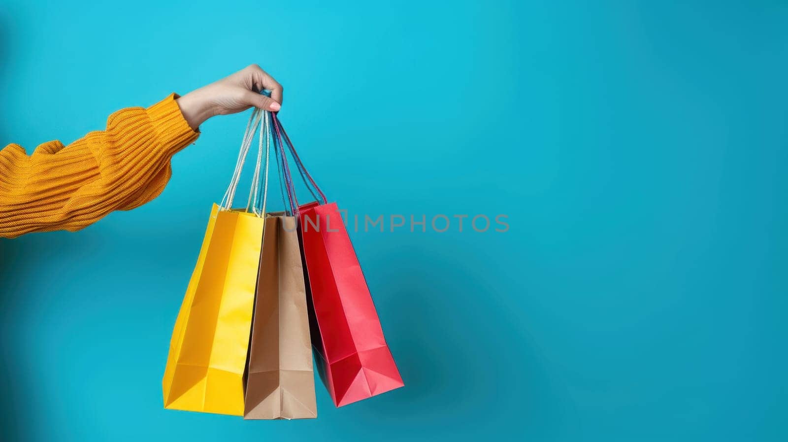 Close up of a woman's hand holding colorful shopping bags isolated on a blue background.