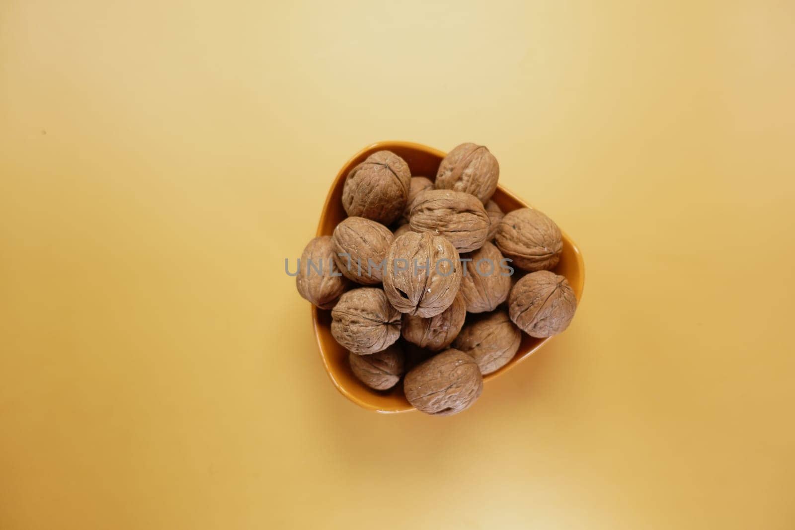 stack of natural walnuts in a bowl on orange color background by towfiq007