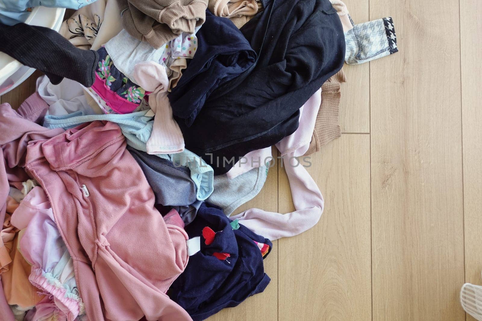 Clothes pile next to laundry basket filled with garments, on hardwood floor.
