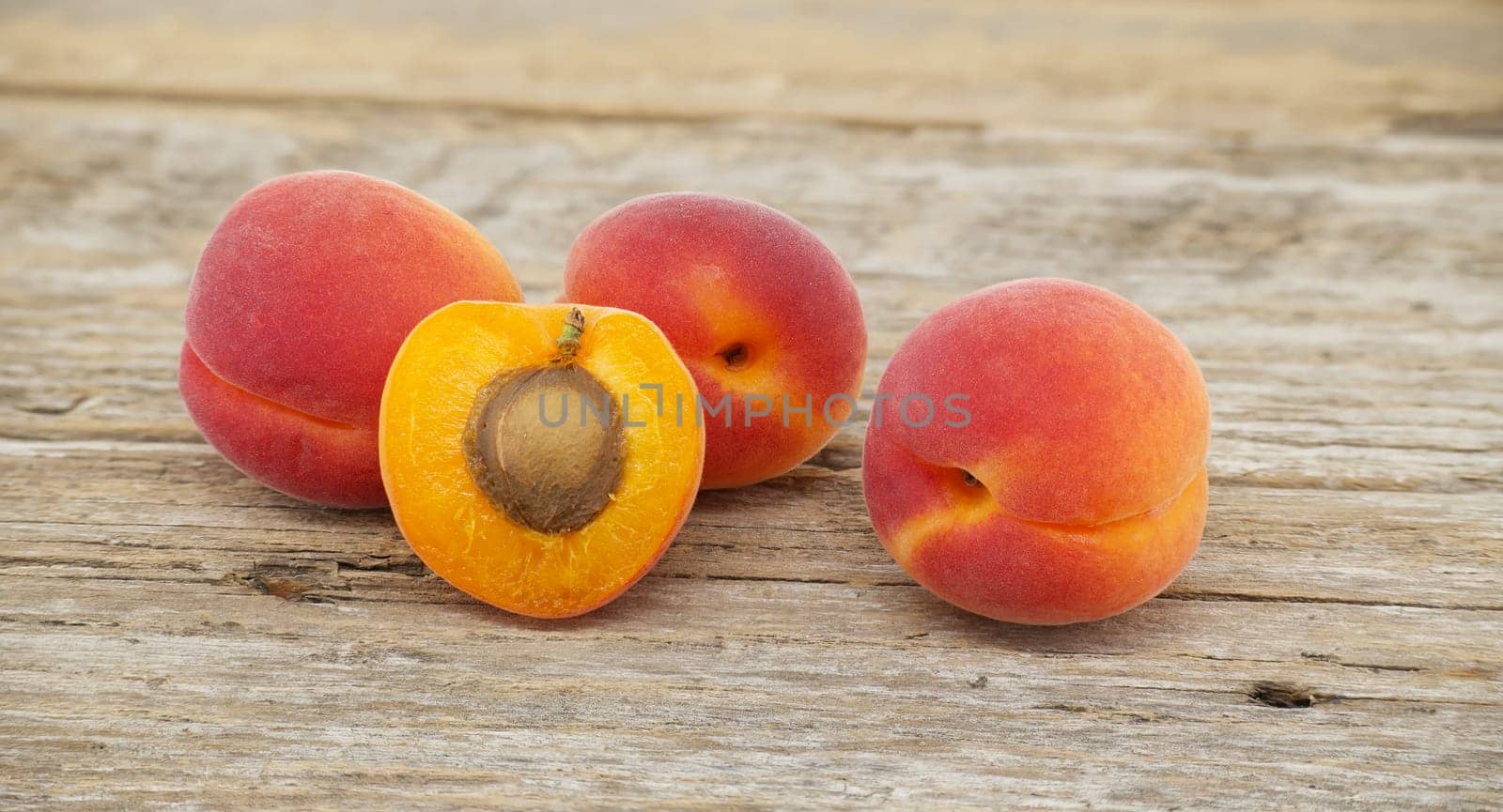 Group of fresh whole apricots and one cut in half to reveal its interior, rustic wooden table