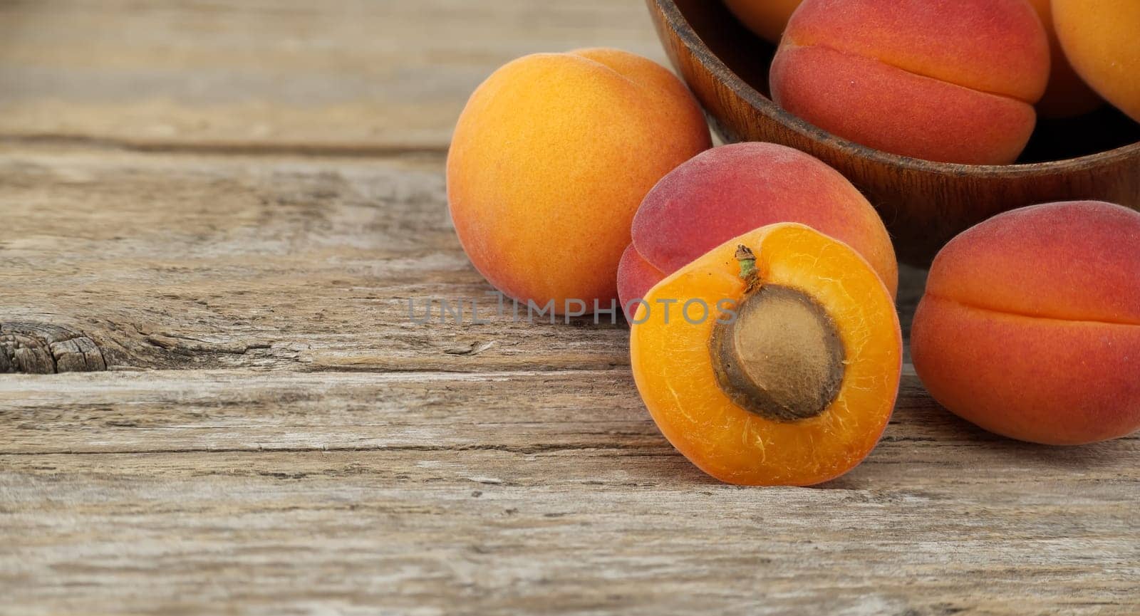 Collection of ripe whole apricots and one cut in half to reveal its interior, rustic wooden table