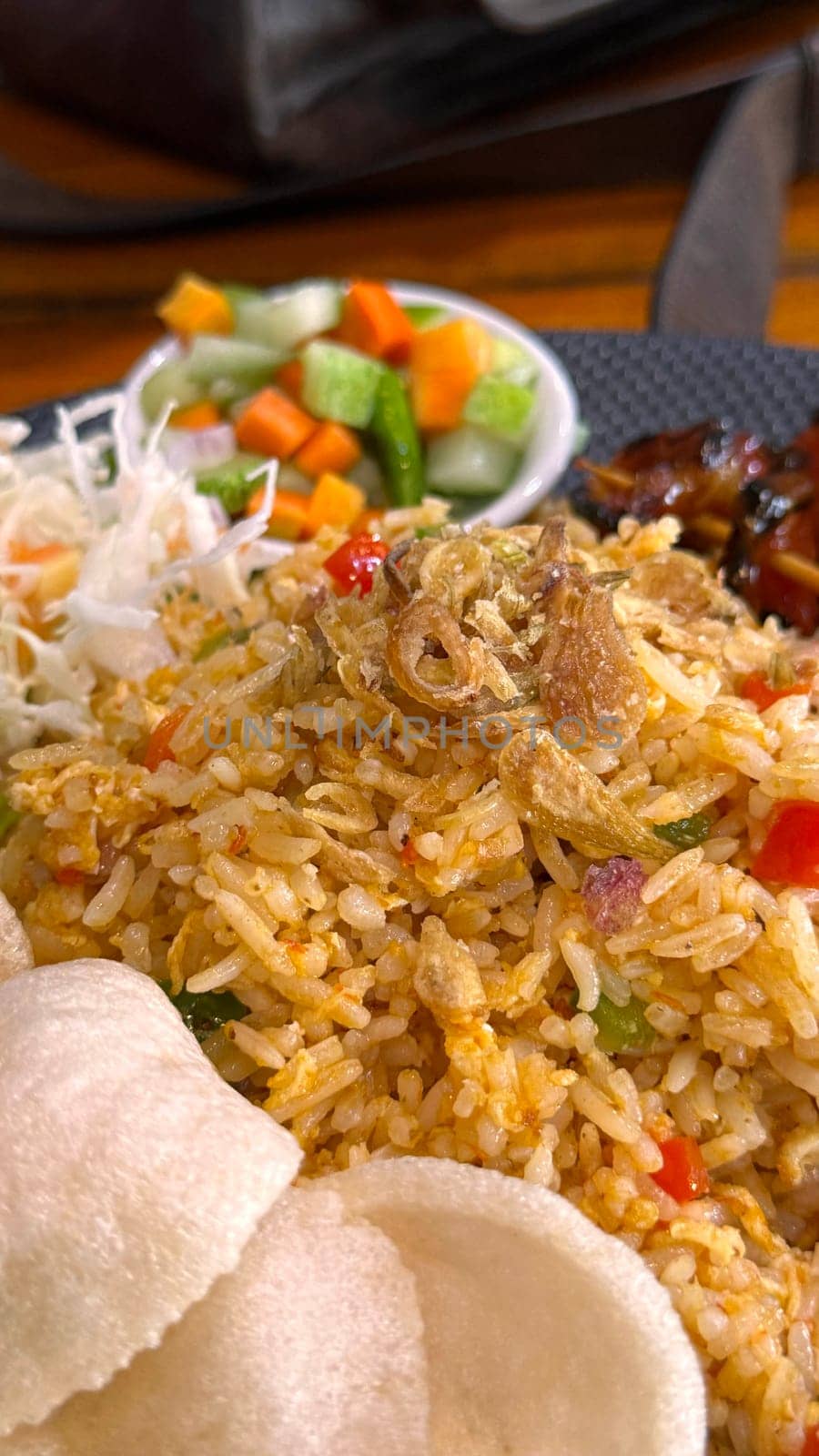 Fired rice or nasi goreng Indonesian chicken fried rice served with pickled cucumber and onion and chili with prawn crackers with satay as condiment on grey plate