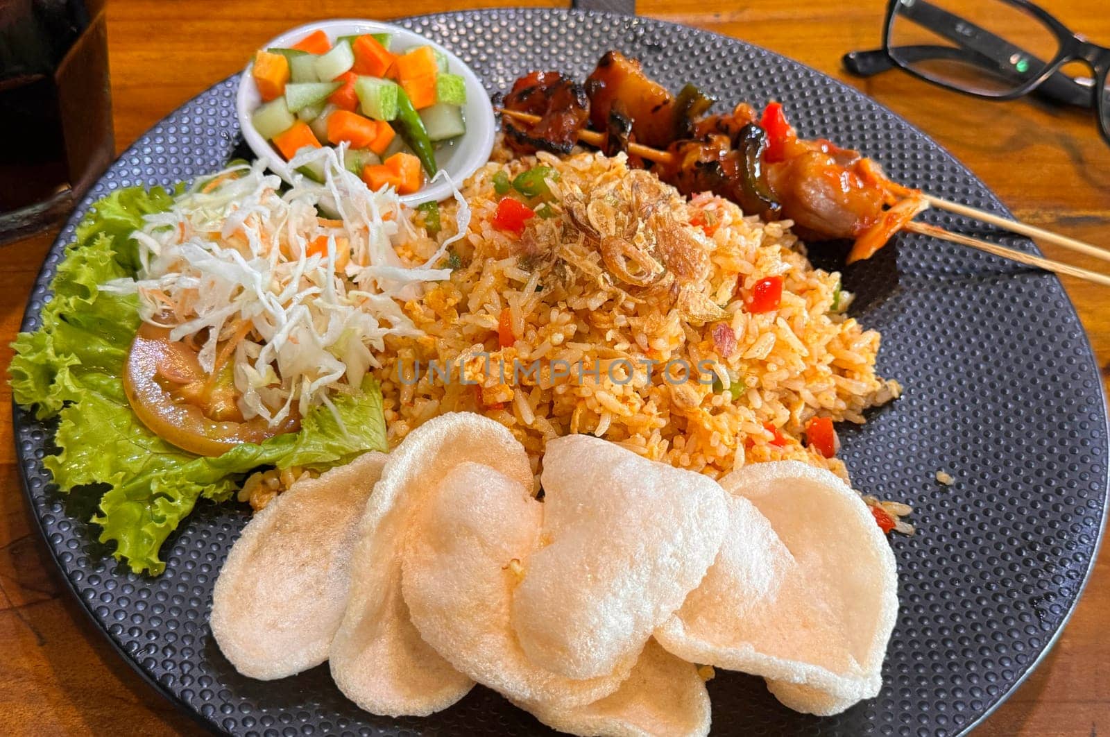 Fired rice or nasi goreng Indonesian chicken fried rice served with pickled cucumber and onion and chili with prawn crackers with satay as condiment on grey plate