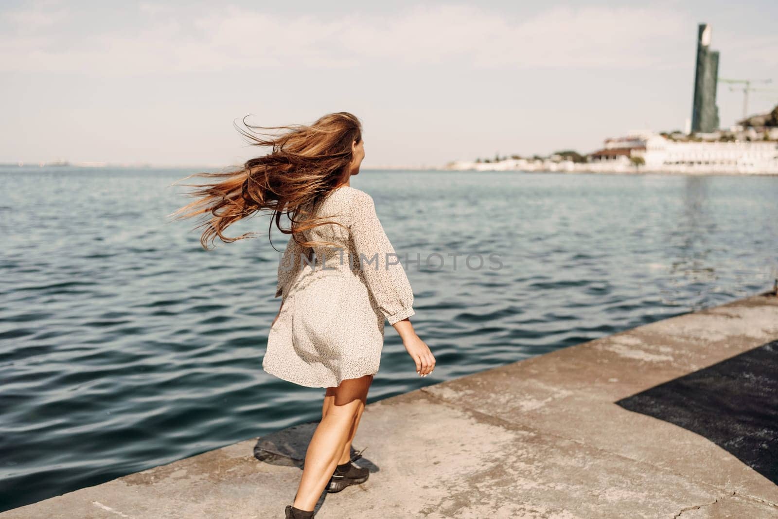 woman in a white dress is walking on a pier near the water. The scene is peaceful and serene, with the woman's long hair blowing in the wind. by Matiunina