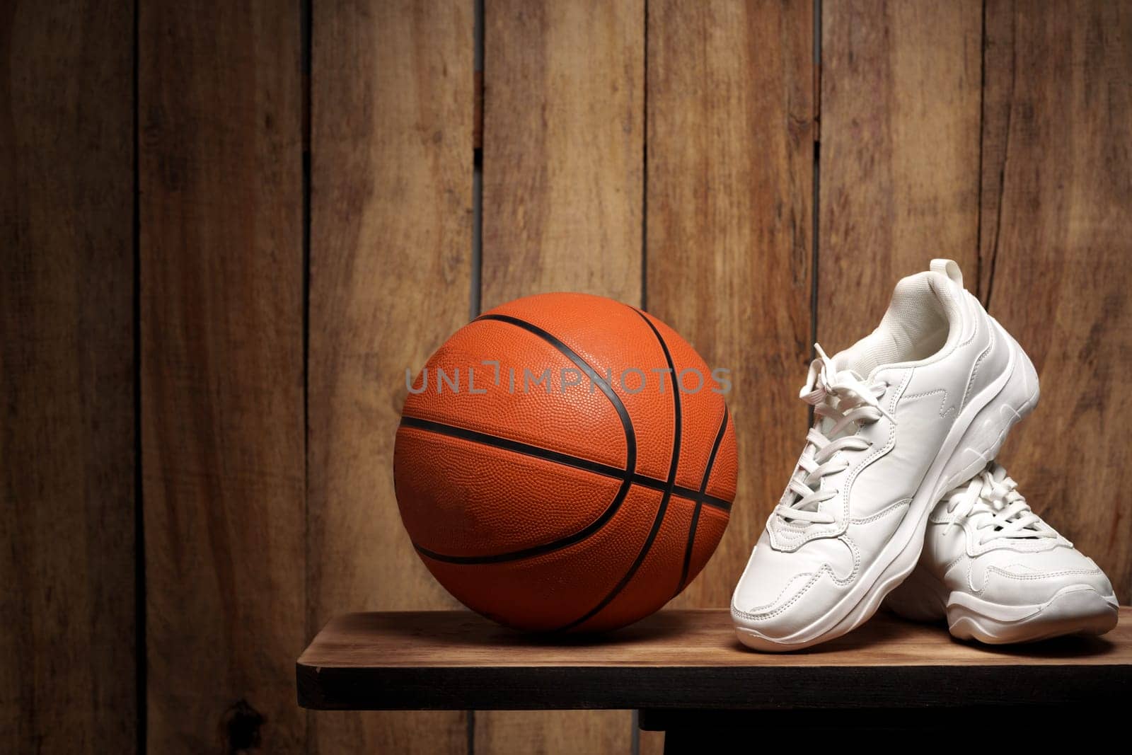 White sneakers and basketball ball against wooden background close up