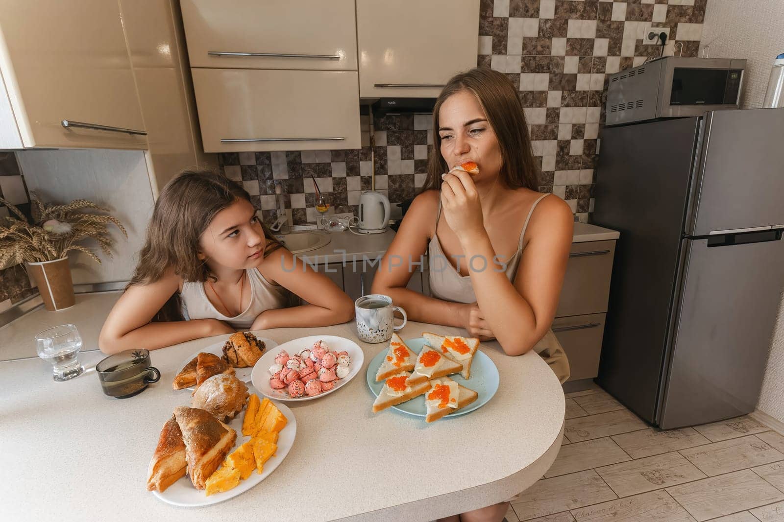 mom and daughter sitting at a table with a variety of food, including sandwiches, fruit, and pastries. They are smiling and enjoying their meal together. by Matiunina