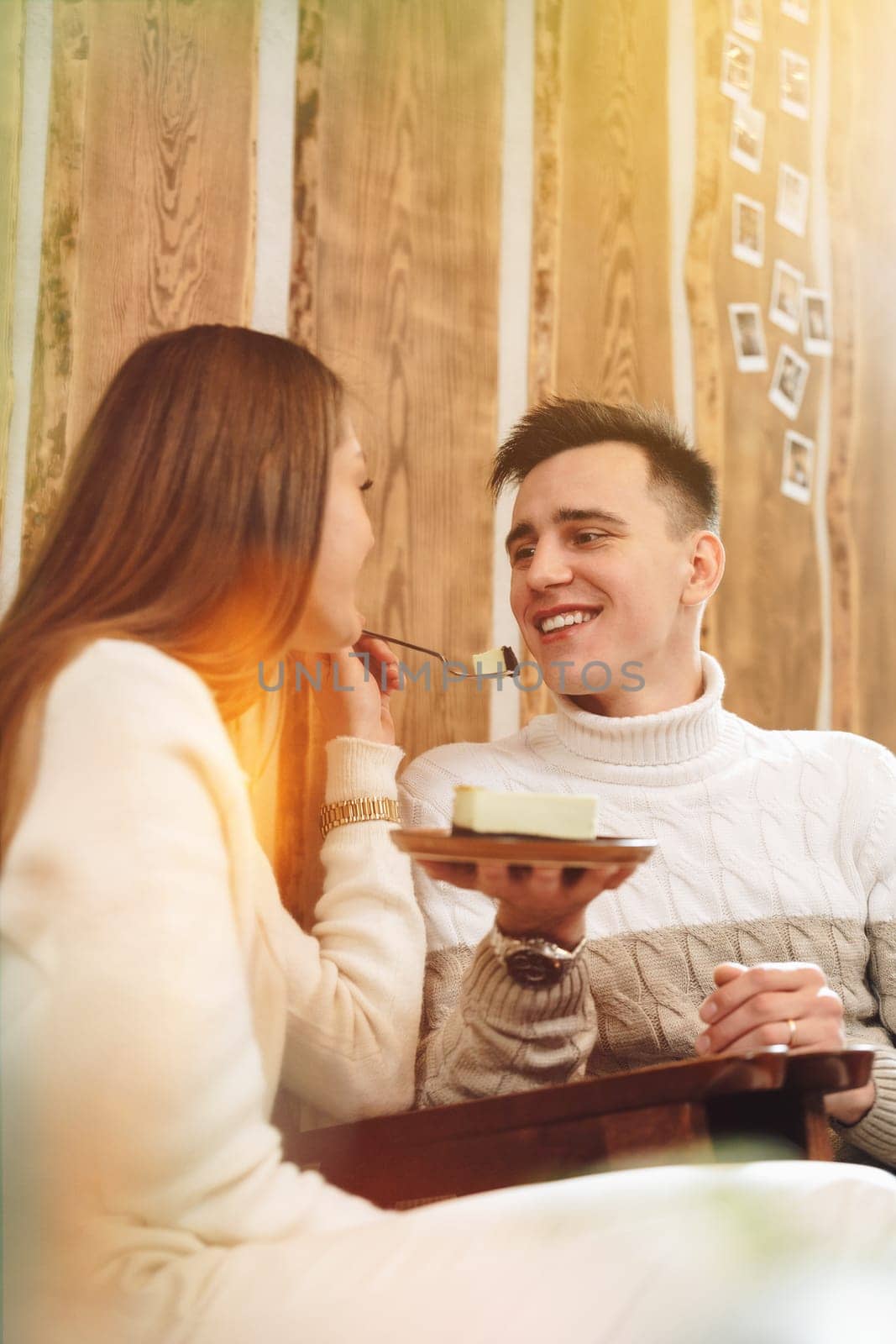 Young Man in White Sweater Enjoying Cheesecake With Friend at Cozy Cafe by Fabrikasimf