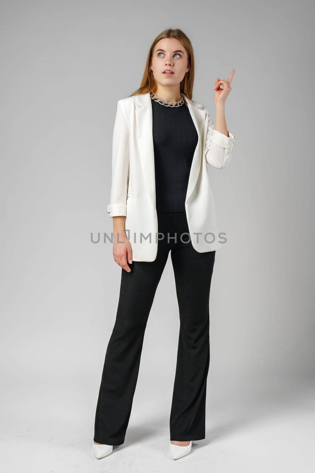 Thoughtful Young Woman in a Stylish White Blazer Posing on gray background by Fabrikasimf