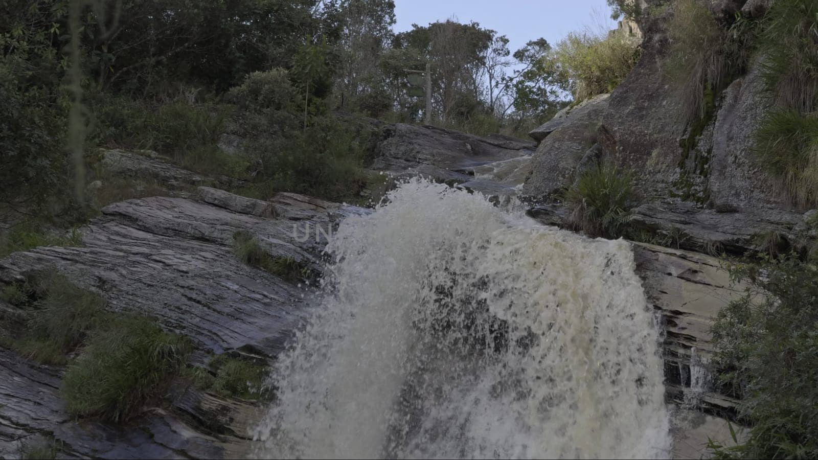 A slow-motion video showcases a tranquil forest waterfall flowing down rocks.