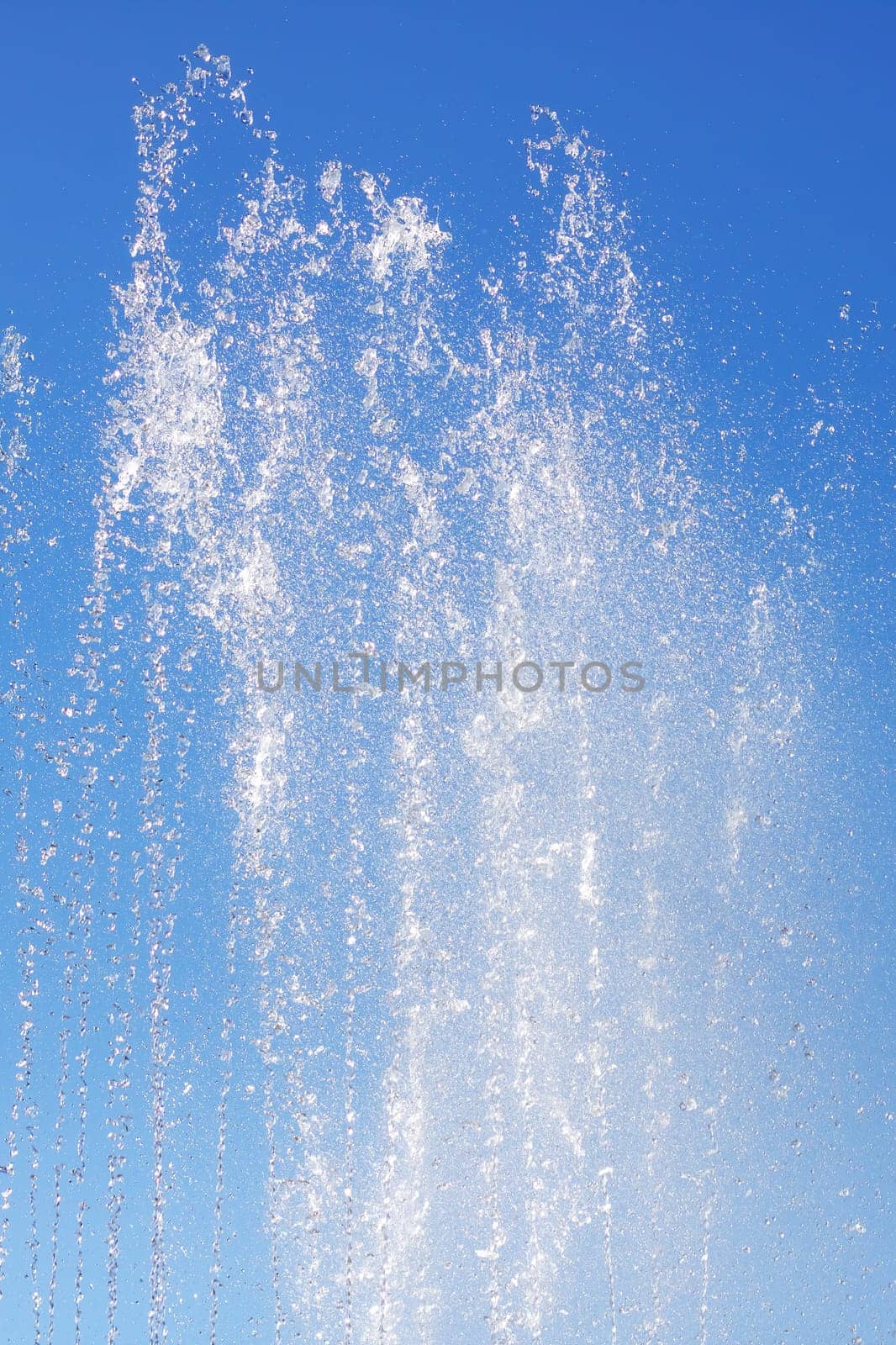 A liquid fountain spraying water against an electric blue sky, creating a stunning natural landscape with trees and clouds in the background