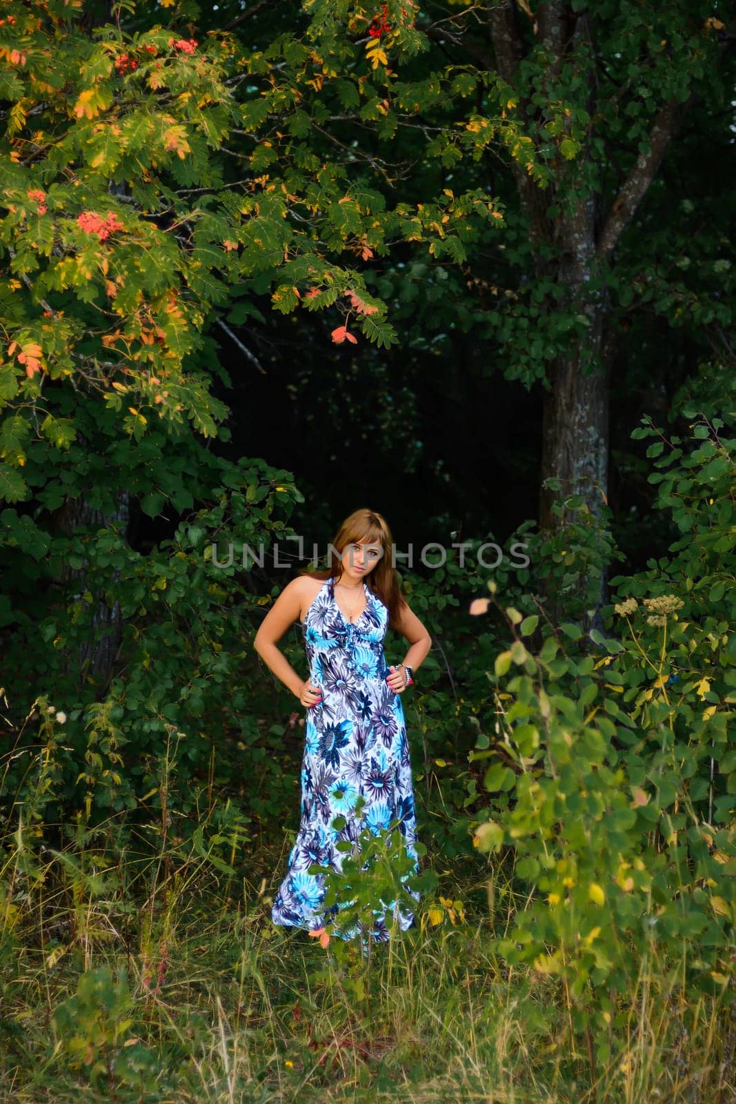 young Caucasian girl in blue dress posing in forest outdoors in summer