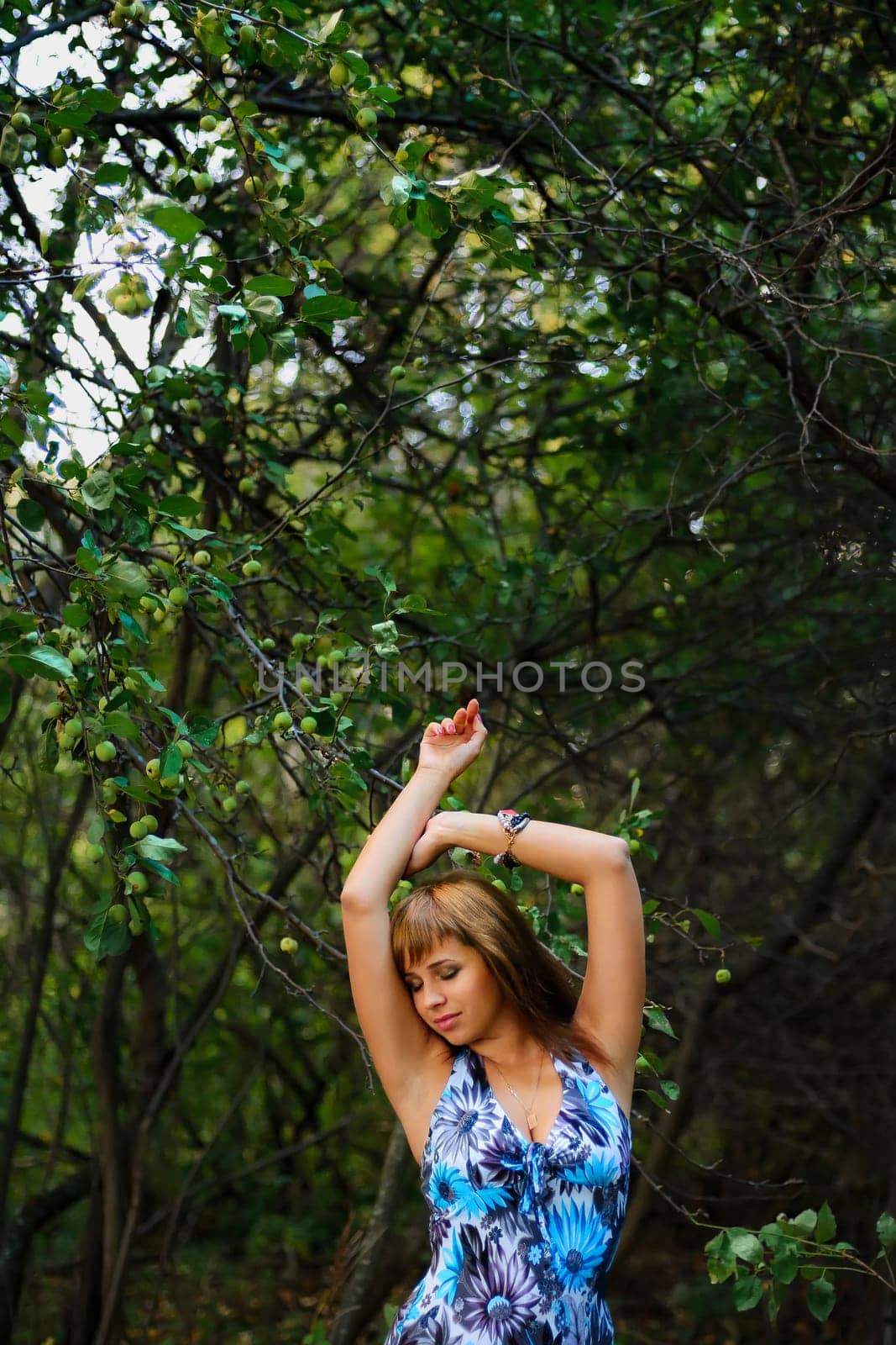 young Caucasian girl in blue dress posing in forest outdoors in summer