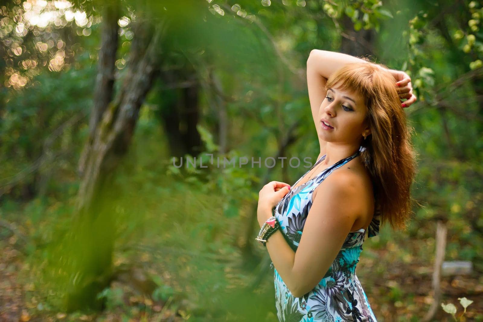 young Caucasian girl in blue dress posing in forest outdoors in summer