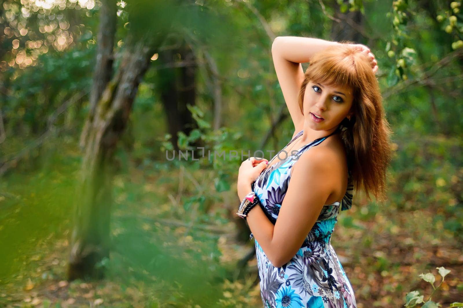 young Caucasian girl in blue dress posing in forest outdoors in summer