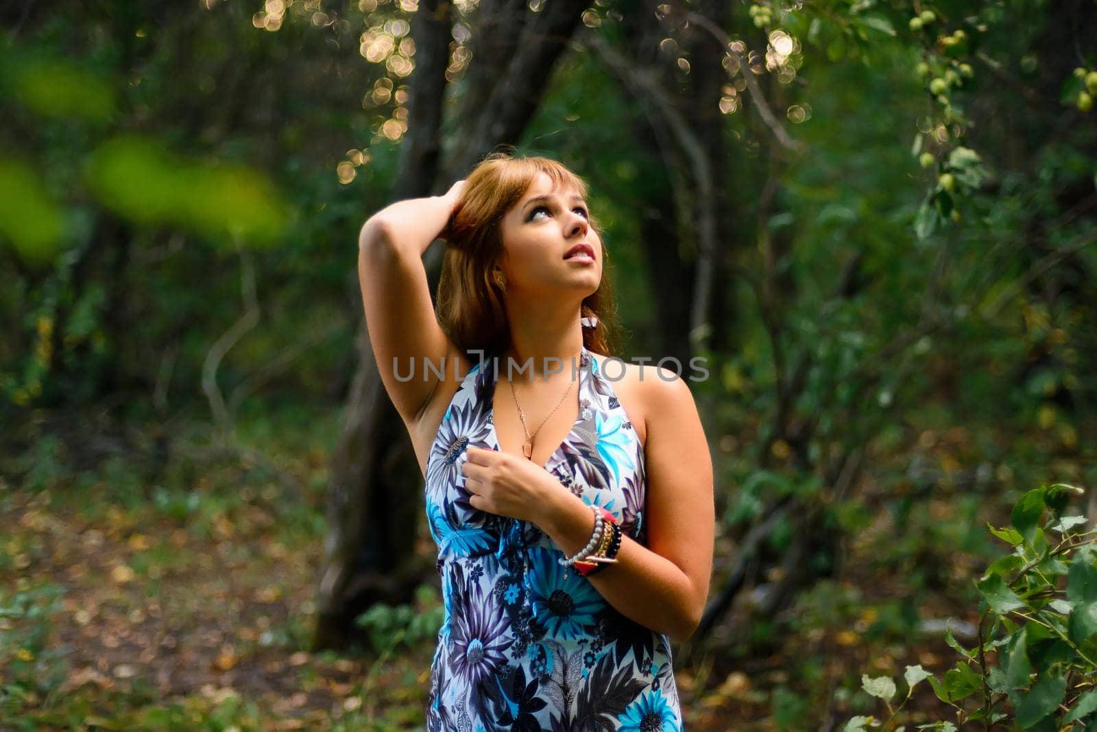 young Caucasian girl in blue dress posing in forest outdoors in summer