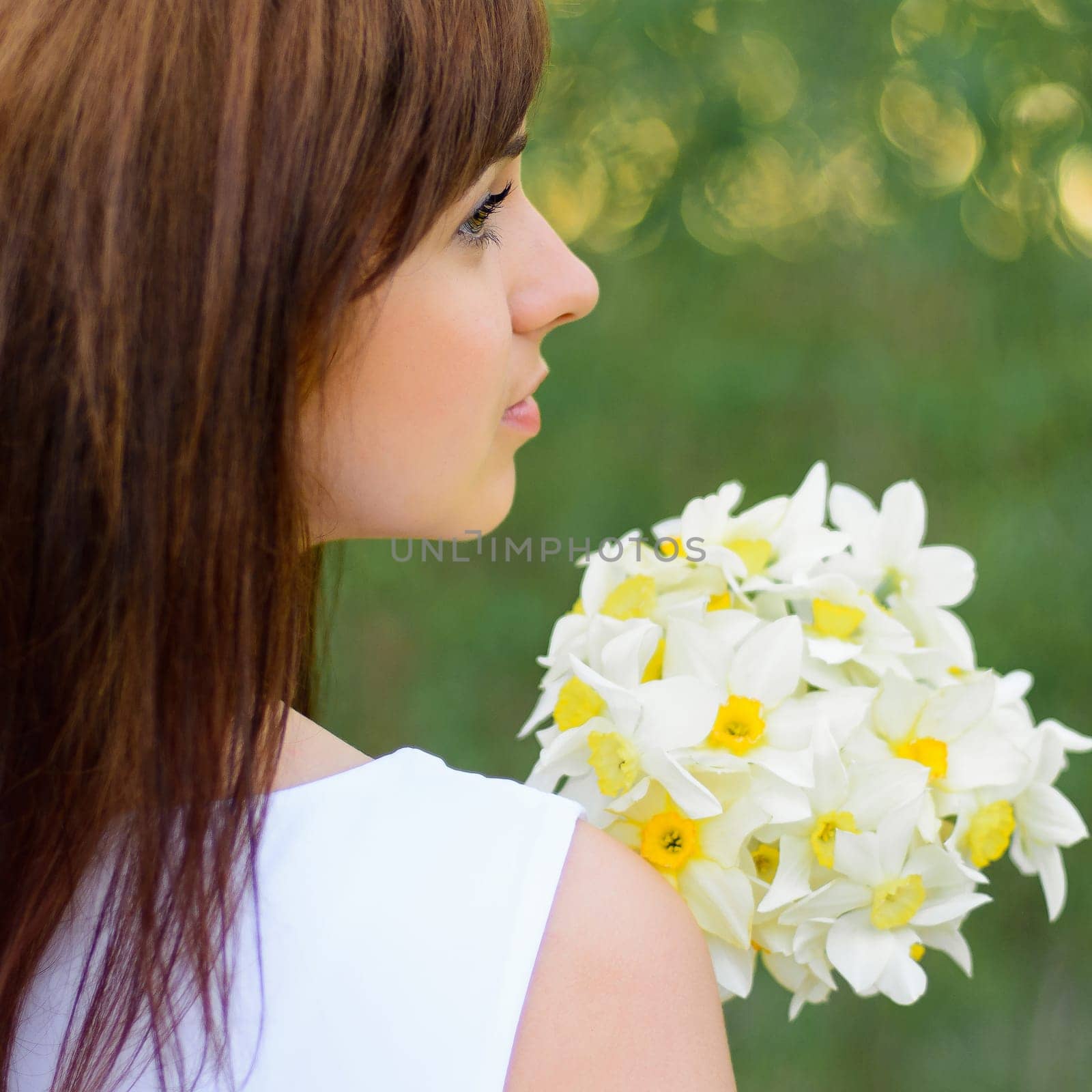 beautiful young girl with a bouquet of daffodils in white dress outdoors in spring
