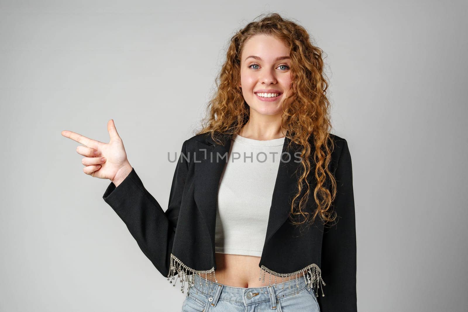 Smiling Young Woman Pointing While Posing in a Studio by Fabrikasimf