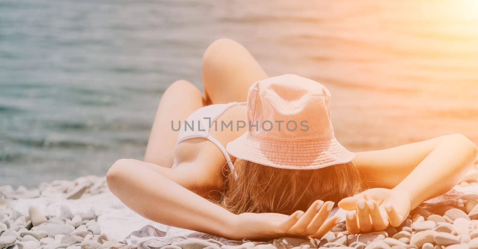 Unrecognizable positive woman in white bikini sunbathing or tanning on seaside beach during summer. Slow motion of happy tourist enjoying sun tan lying on beach chair lounge at luxury resort by panophotograph