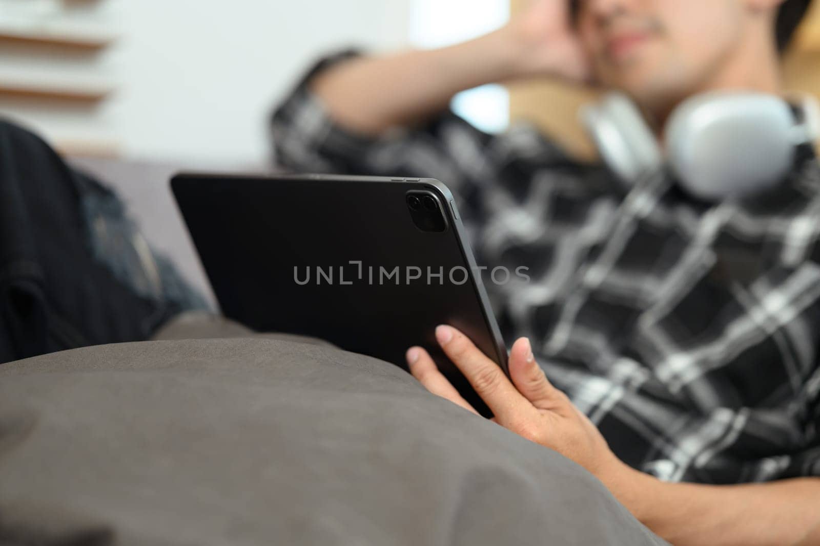 Carefree young man lying on couch and watching movie on digital tablet at home.