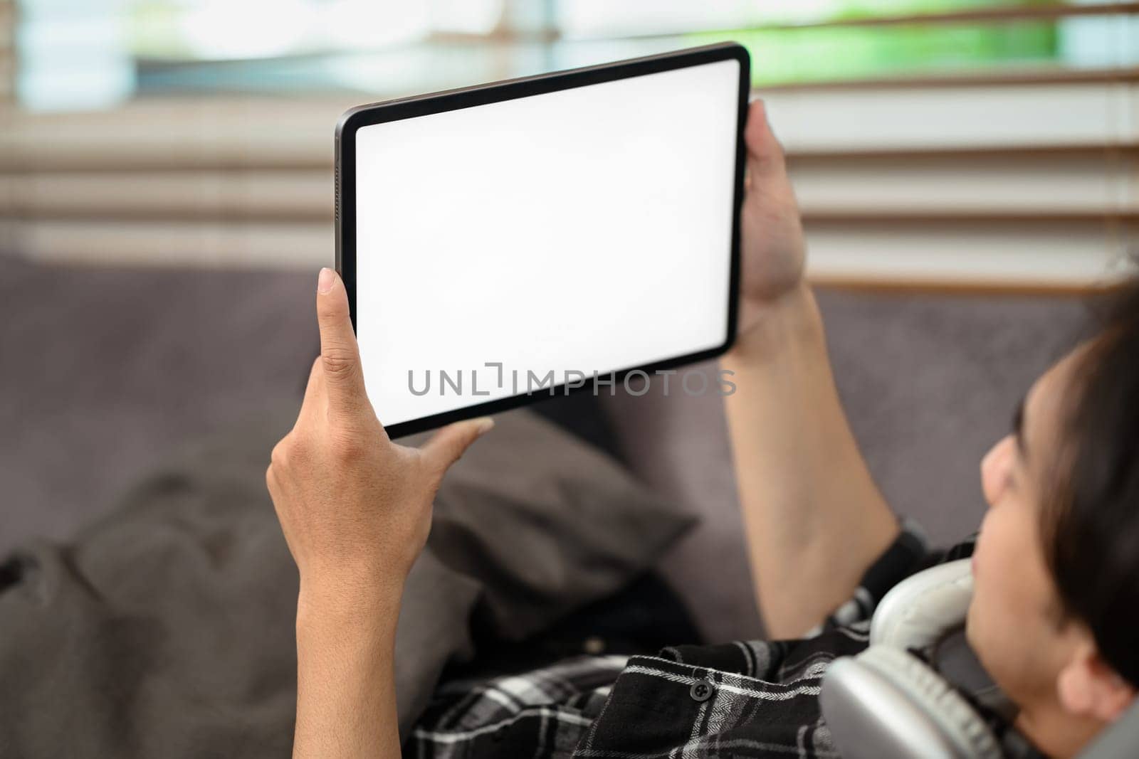 Man holding digital tablet with blank desktop screen lying on couch by prathanchorruangsak