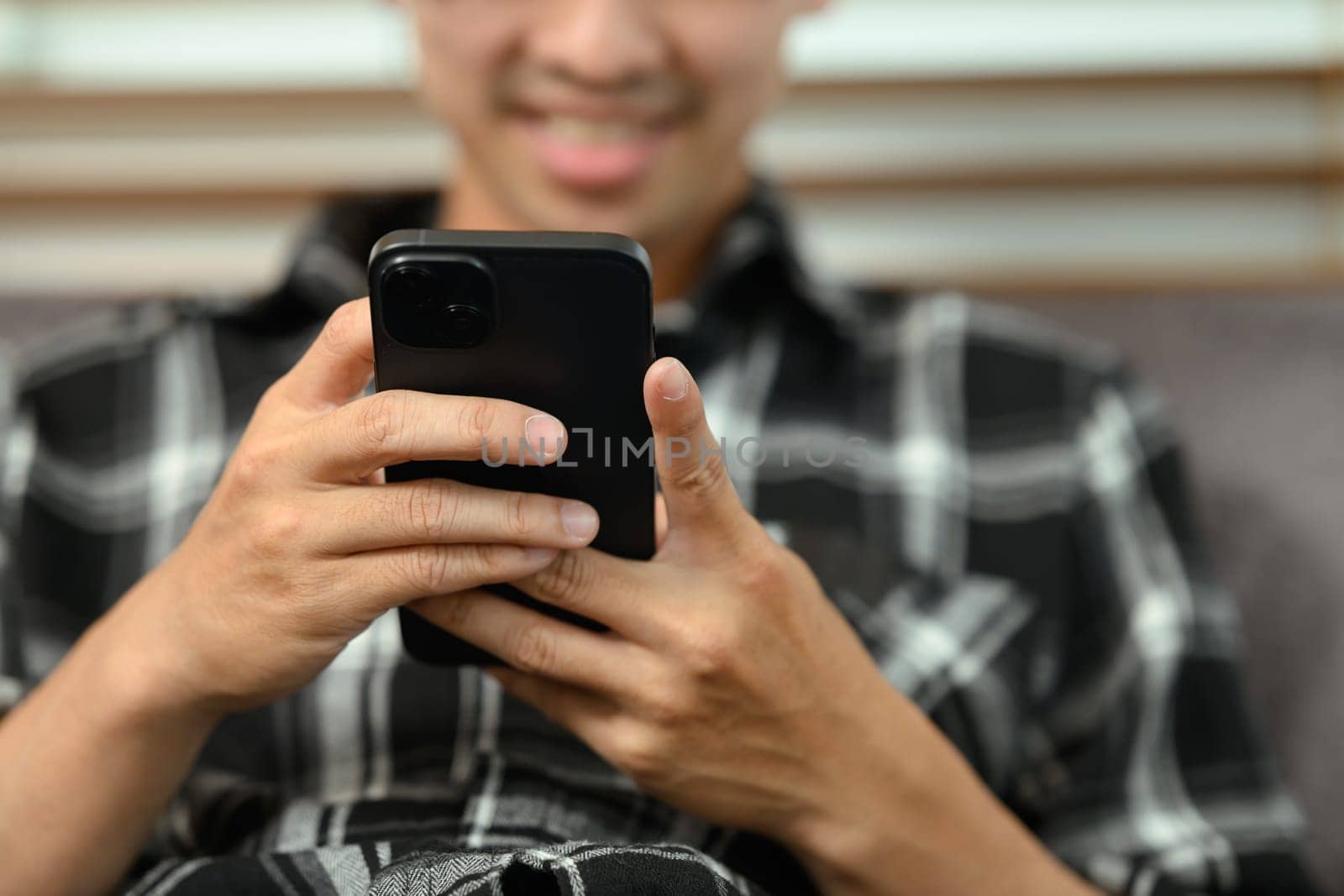 Smiling young man chatting in mobile apps while sitting on couch.