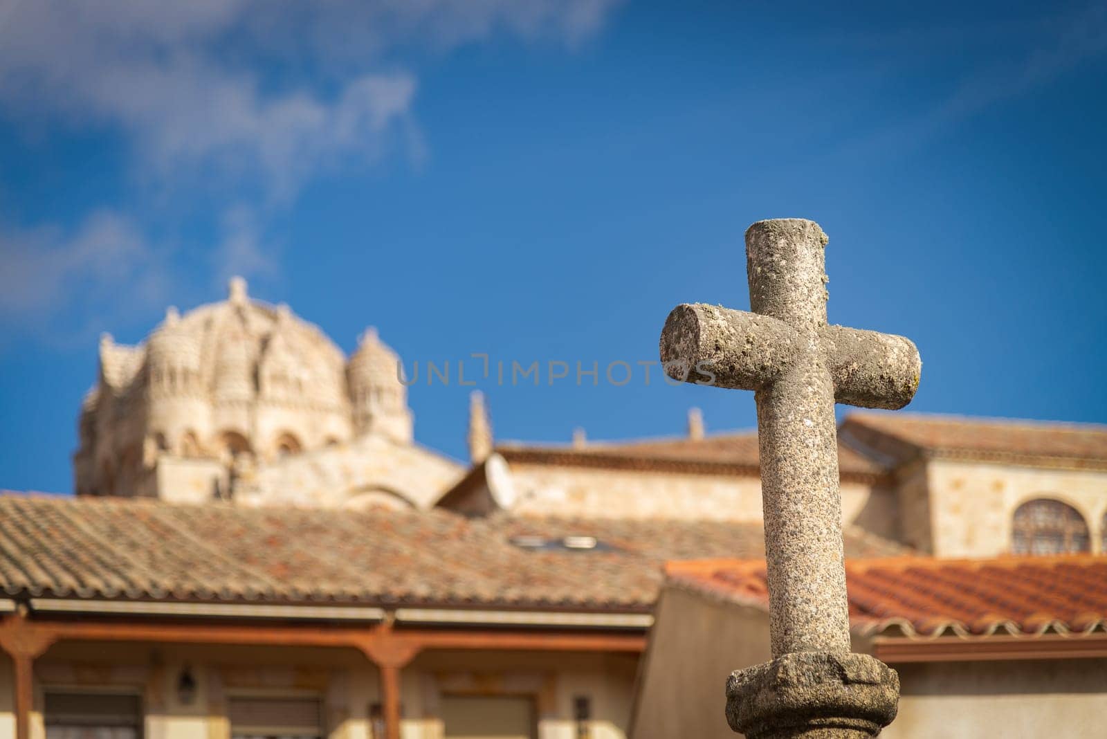 A stone cross in the foreground at San Claudio de Olivares square with the dome of the Romanesque Zamora Cathedral subtly blurred in the background.