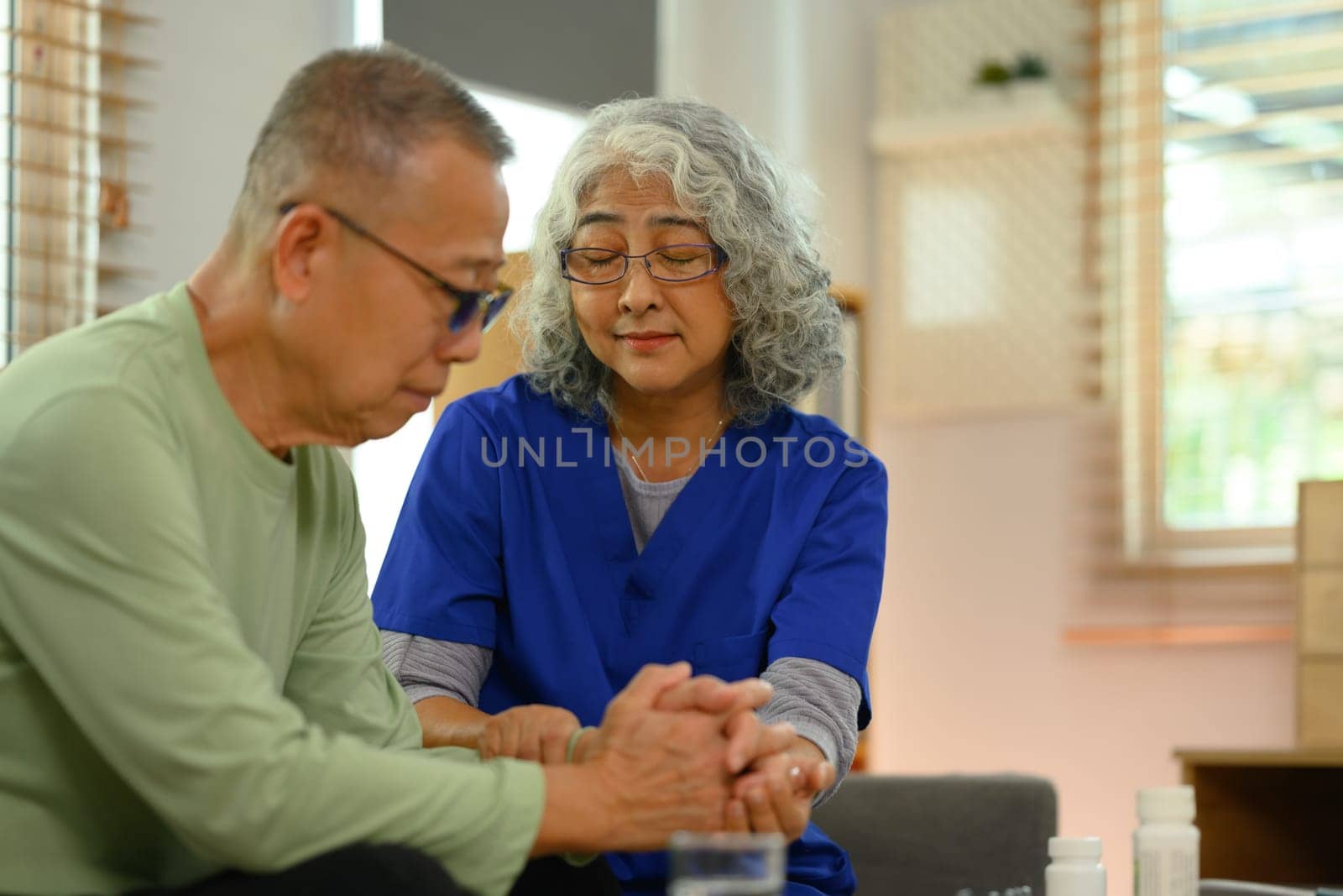 Positive female doctor holding senior patient hand, giving support during home visit.