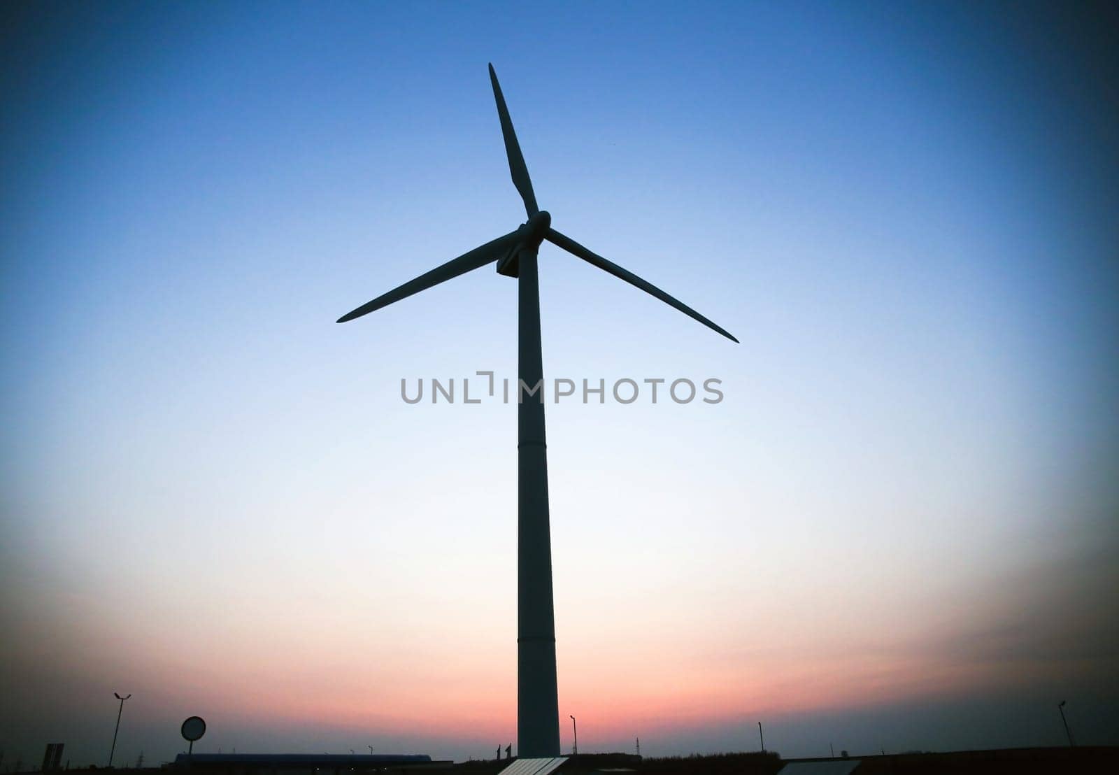 A wind turbine stands tall, its blades still against the blue sky, creating a striking silhouette on the horizon.