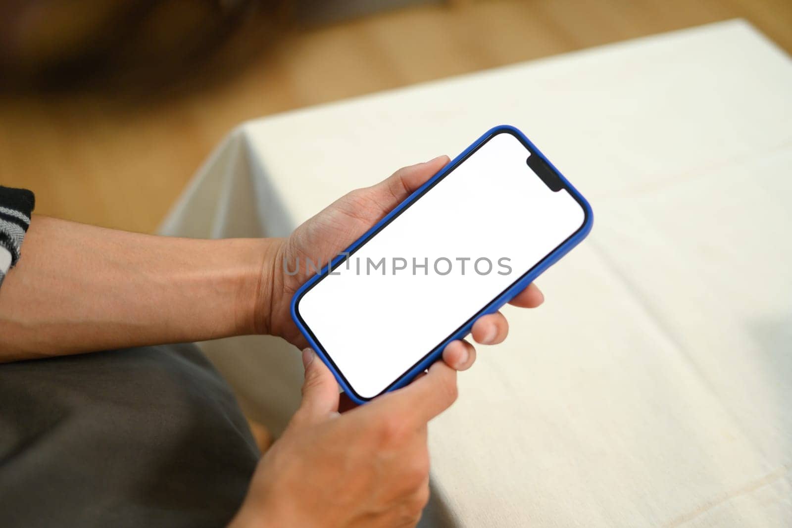 Unrecognizable man hands holding mobile phone with empty screen sitting on couch.