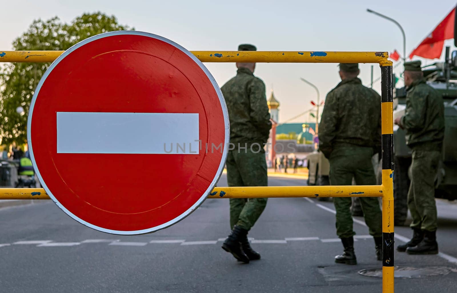 Armed soldiers at a roadblock with a no entry sign. Soldiers in full gear, carrying rifles. Roadblock made of metal barriers. No entry sign is large and red with a white border.