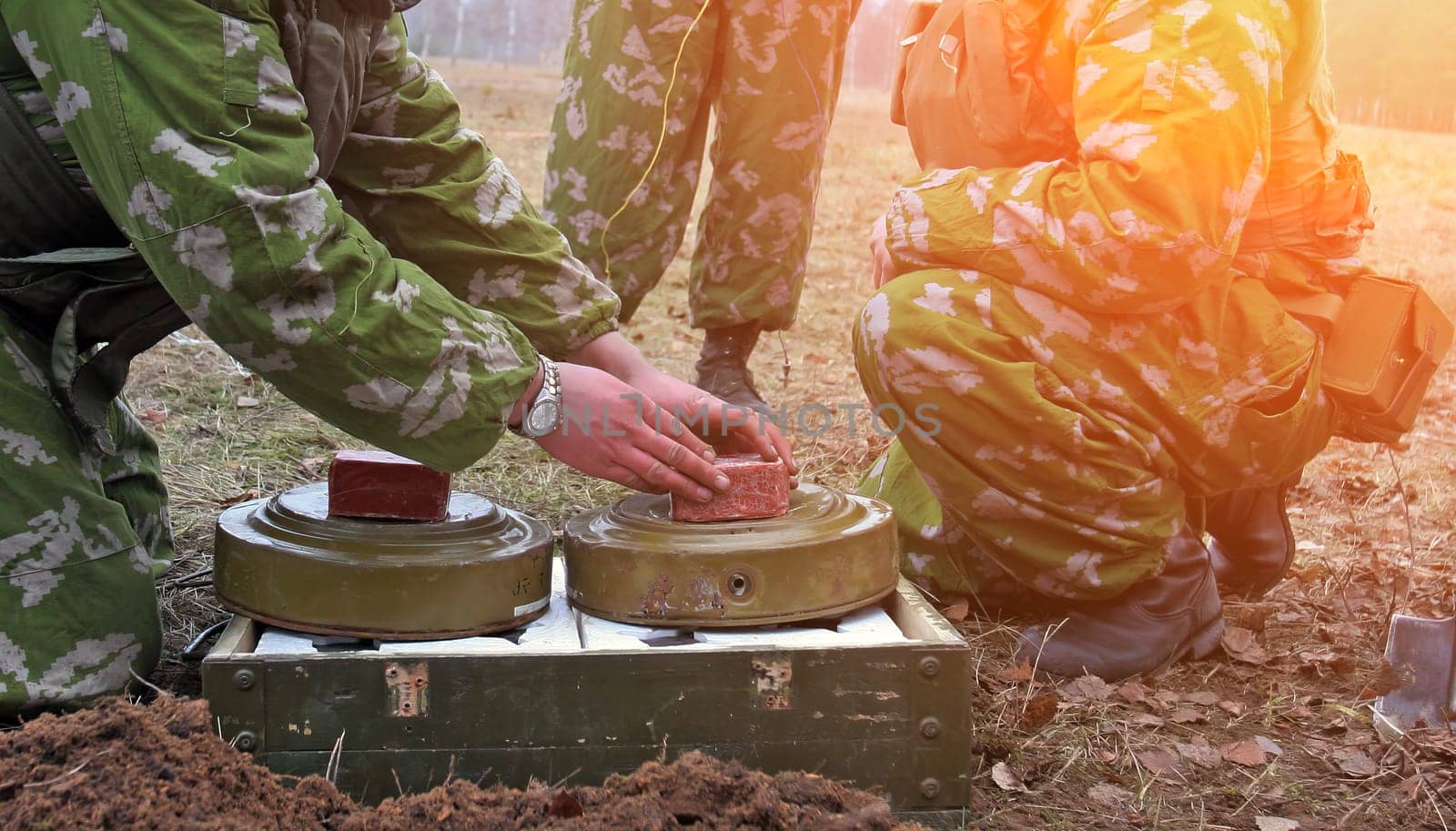 Soldiers in camouflage planting land mines in a war-torn field. Strategic placements deter enemy. Focused soldiers seen from a low angle with rifles. Portrays the gravity of military defense.