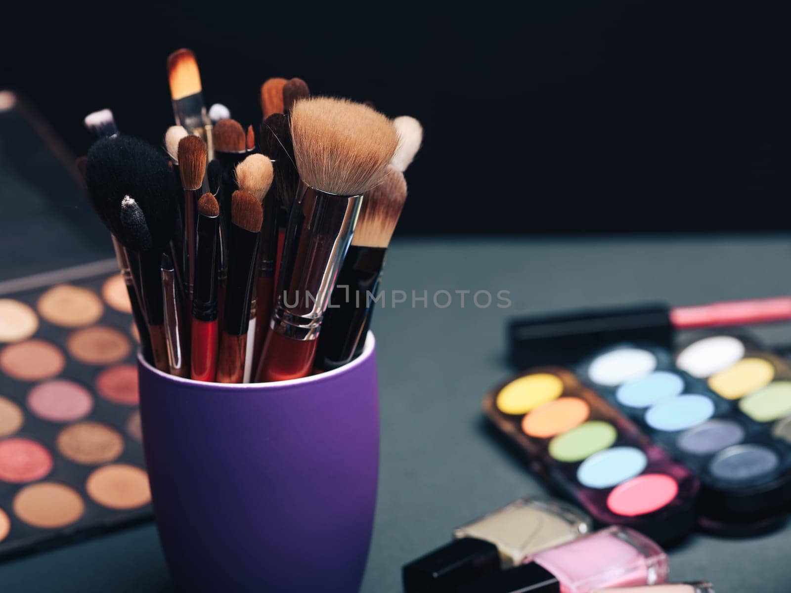 set of professional makeup brushes on the background of a palette with colored eye shadows and other cosmetics for women's beauty