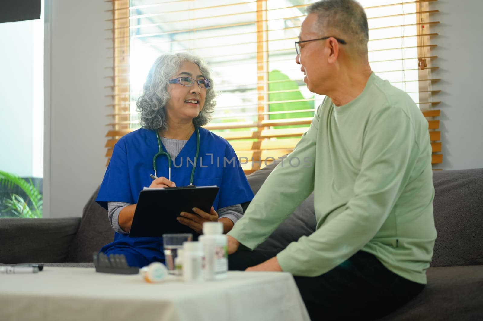 Positive general practitioner taking notes and communicating with elderly patient at home.